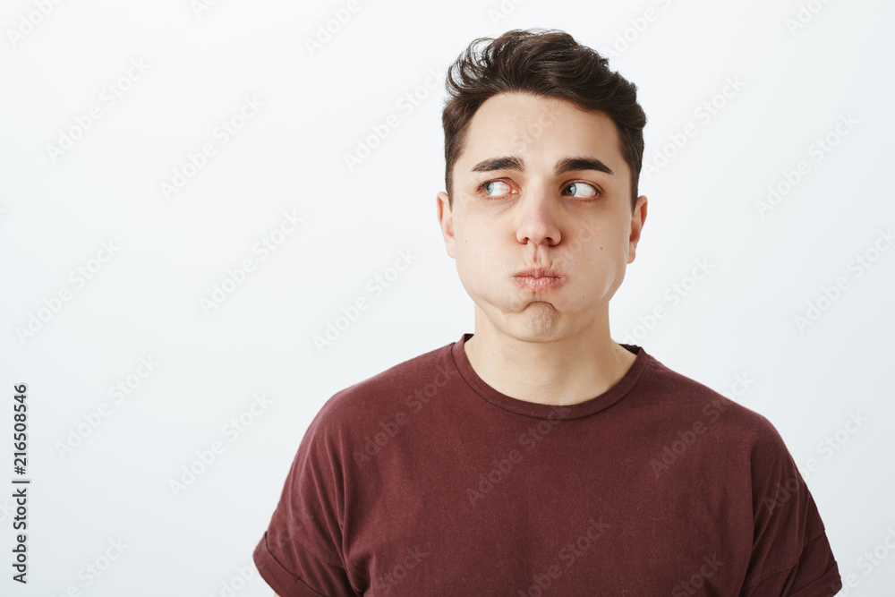 Portrait of funny european male model in red t-shirt, holding breat, sulking and looking left while holding water in mouth, standing over gray background during appointment in dentist office Portrait of funny european male model in red t-shirt, holding breat, sulking and looking left while holding water in mouth, standing over gray background during appointment in dentist office