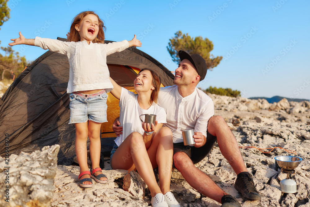 Family resting near tent, little girl standing and holding hands up. Family resting near tent, little girl standing and holding hands up.
