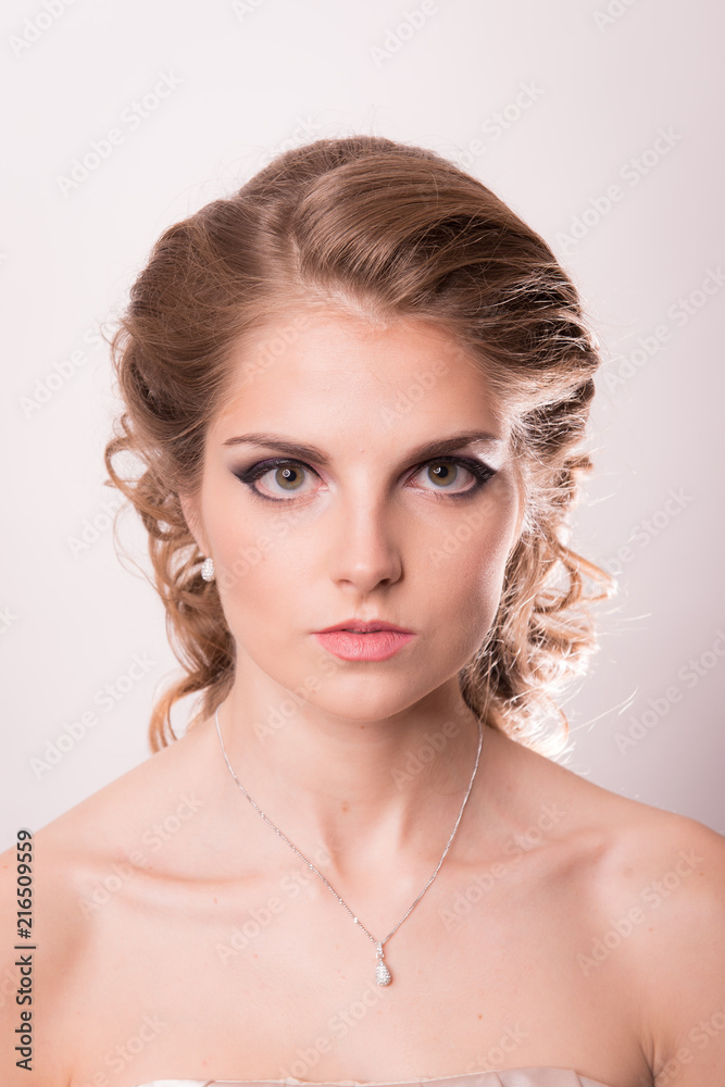Brown-haired woman with a wedding hairstyle and make-up against a vintage wall background close up.