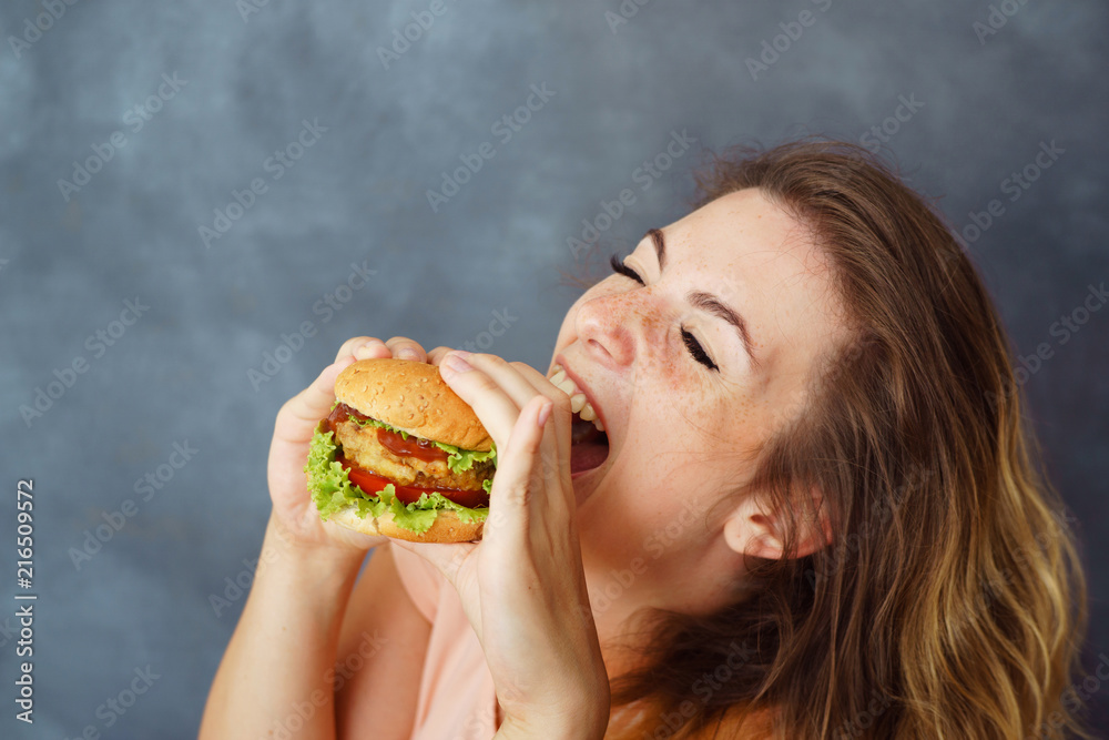 Pleasure, delight, enjoyment, treat, happiness, appetite, fast food, hunger. Cute young woman eating delicious burger enjoying the taste Pleasure, delight, enjoyment, treat, happiness, appetite, fast food, hunger. Cute young woman eating delicious burger enjoying the taste