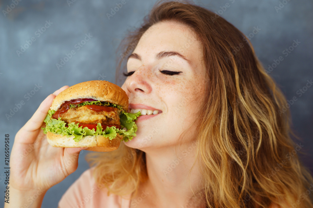 Pleasure, delight, enjoyment, treat, happiness, appetite, fast food. Cute young woman eating greedily delicious burger expressing enjoyment with its taste Pleasure, delight, enjoyment, treat, happiness, appetite, fast food. Cute young woman eating greedily delicious burger expressing enjoyment with its taste