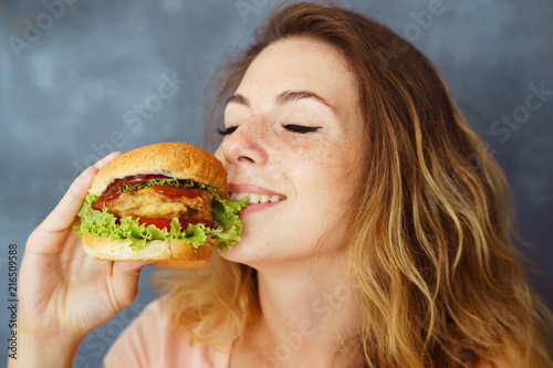 Pleasure, delight, enjoyment, treat, happiness, appetite, fast food. Cute young woman eating greedily delicious burger expressing enjoyment with its taste