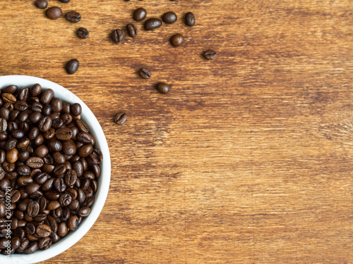 Macro shot of coffee beans on wooden background and coffee in white bowl, flat lay, copyspace