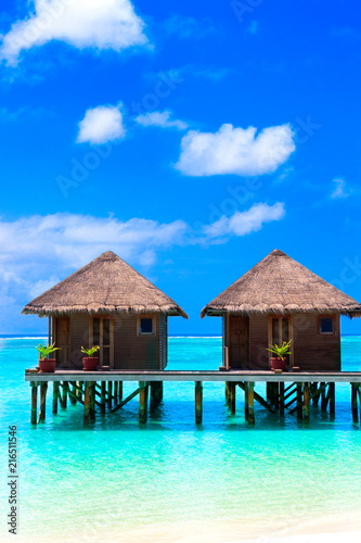 Water villas on wooden pier in turquoise ocean on the white sand beach