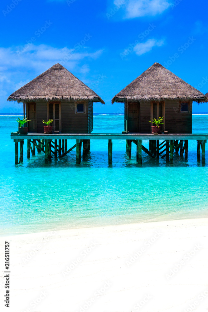 Water villas on wooden pier in turquoise ocean on the white sand beach