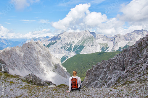 Hiker with backpack sitting on top of the mountain and enjoying the valley view at sunny day. Girl, Austrian Alps. 
