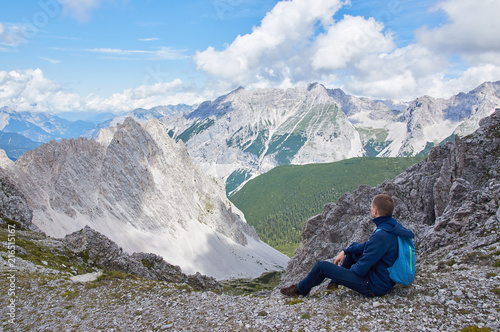 Hiker with backpack sitting on top of the mountain and enjoying the valley view at sunny day. Man, Austrian Alps. 