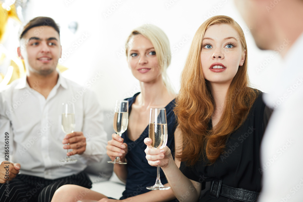 Young woman with flute of champagne talking to one of her friends at party Young woman with flute of champagne talking to one of her friends at party