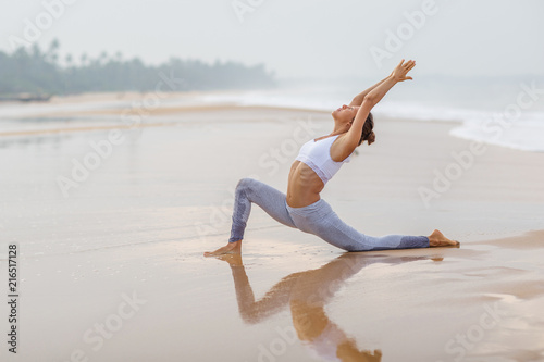Caucasian woman practicing yoga at seashore of tropic ocean