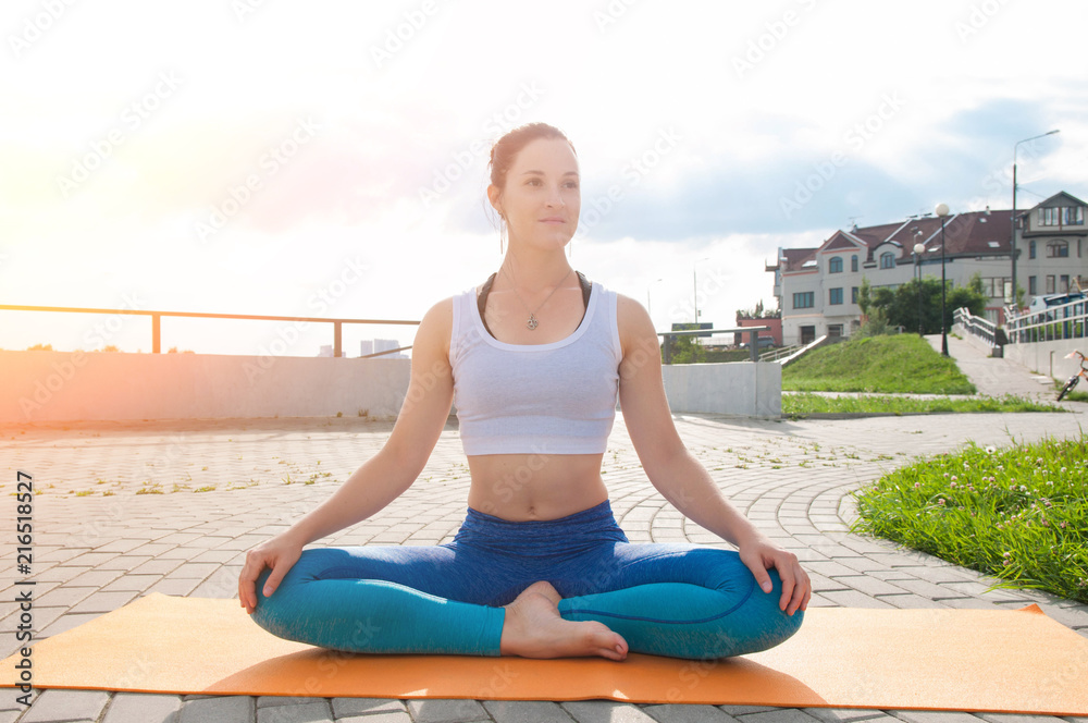 Fototapeta premium Young pretty woman practices yoga and meditates on the sunny embankment of the river