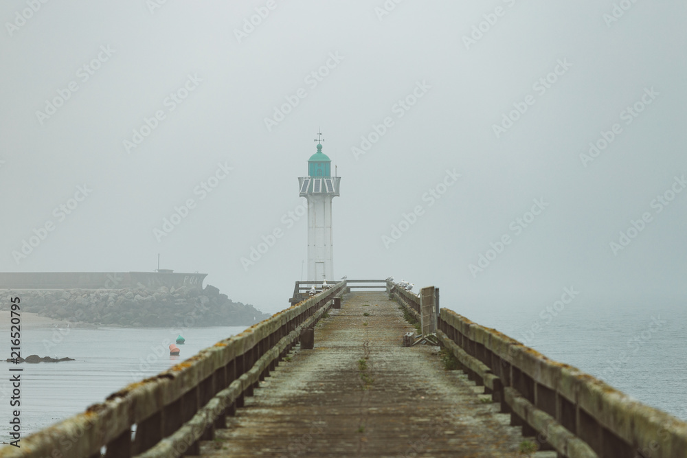 Pier and lighthouse in the harbour of Deauville on a misty morning in Normandy, France. English channel seascape