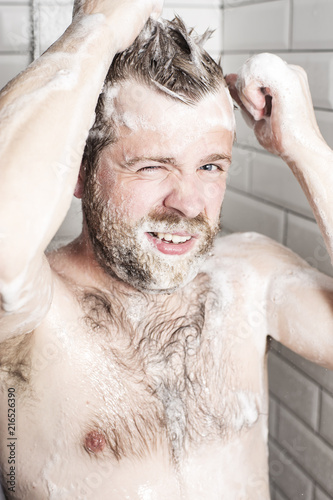 Attractive bearded man washing her hair in the shower under running water.
