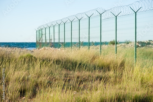 state border danger zone with high fence with razor wire on empty sea coast