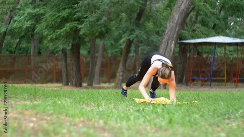 Young Athlete Woman in Sport Outfit Engaged Fitness Lying on a Carpet in a Park on a Green Lawn. The girl does sports exercises and workout on stadium background. Fitness female doing skipping workout photo