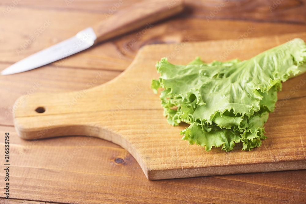 Lettuce leaves on cutting board with knife on wooden background. Lettuce leaves on cutting board with knife on wooden background.