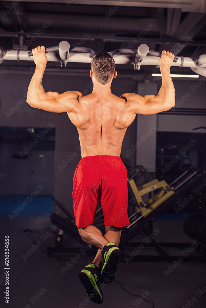 Naklejka premium Strong young man doing pull up exercise on horizontal bar in gym