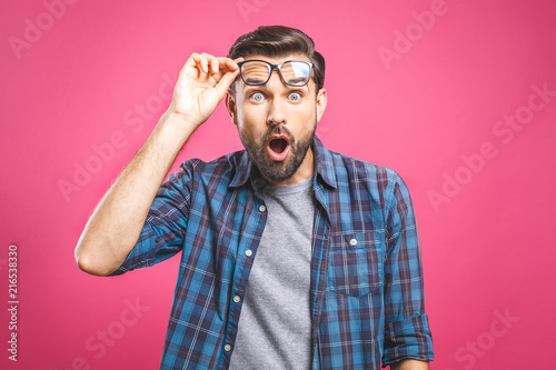 OMG! It's incredible! Portrait of handsome young man in glasses looking at camera while standing against pink background. Close up portrait of bearded man keeping his mouth open.