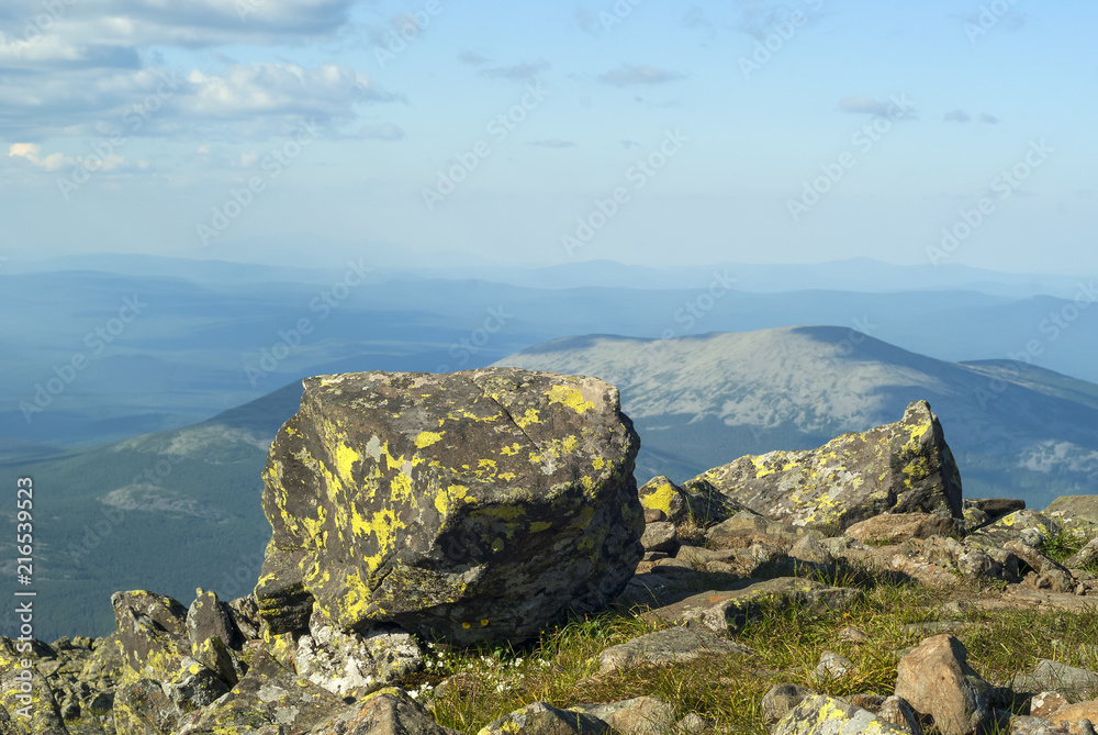 view from the top of Mount Konzhakovskiy Kamen - section of mountain tundra with lichen-covered rocks and a view of the wooded mountains to the horizon..