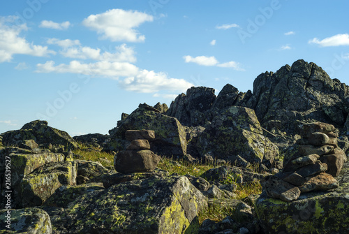 stone pyramid - a road sign for the designation of a trail in the fog - in a beautiful mountainous wild terrain with picturesque rocks under a blue sky photo