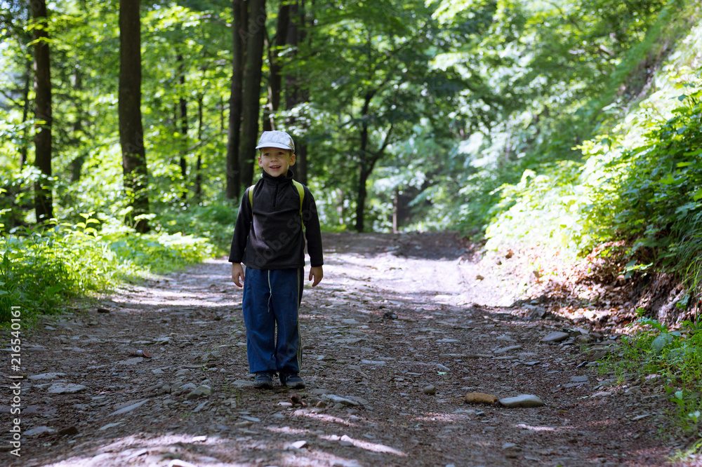 Obraz premium Portrait of cheerful caucasian little boy in summer with big blurry background, scene on a trip in the woods.