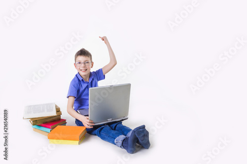 Portrait of cute schoolboy sitting with books and typing on laptop keyboard © Solarisys