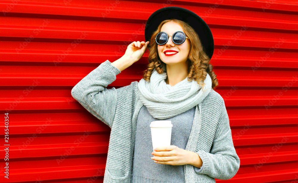 Stylish autumn portrait smiling woman with coffee cup is wearing a knitted clothes on a red background