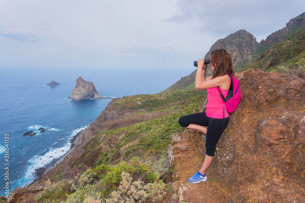 Hiker woman on top of the mountain looking through binoculars