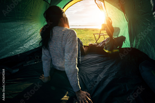 An Asian woman sitting in the tent in font of the lake camping site on weekend holiday. Travel relaxing and adventure concept.