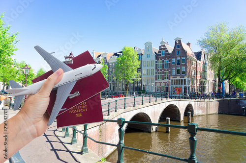 Plane travel concept, hand holding passports with plane over Amsterdam background