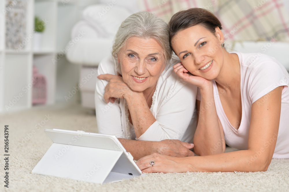 Mother and her adult daughter lying on floor and looking at tabl Mother and her adult daughter lying on floor and looking at tabl