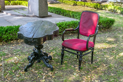 Empty Vintage antique black wooden table and antique velvet red armchair in the garden, park against the background of grass and trees, outdoor rest, furniture set in garden, living area decoration