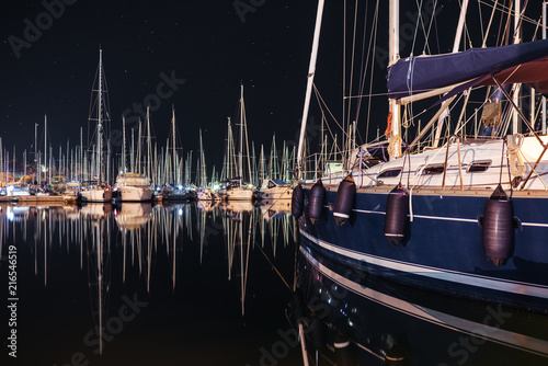 Many yachts sail boats in marina bay at night mirroring in a sea