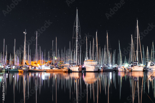 Many yachts sail boats in marina bay at night mirroring in a sea