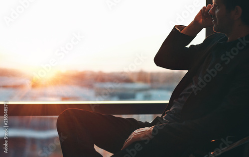 Businessman on the phone whilst sitting at the window at sunset
