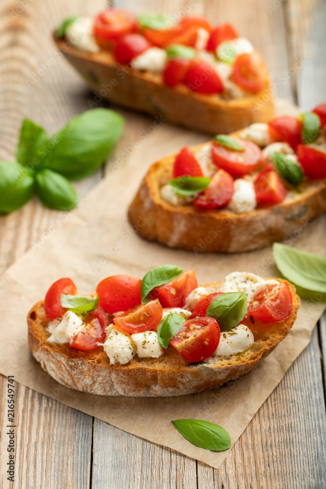 Bruschetta with tomatoes, mozzarella cheese and basil on a old rustic table. Traditional italian appetizer or snack, antipasto