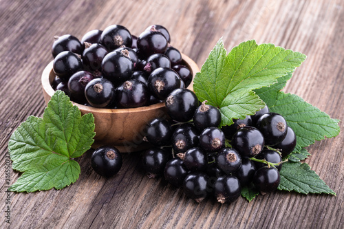 Fresh ripe black currant in wooden bowl with original leaves on rustic old background photo