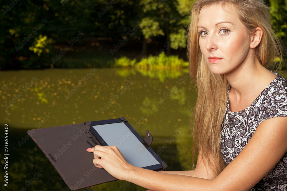 Fototapeta premium Woman sitting in park, relaxing and using tablet