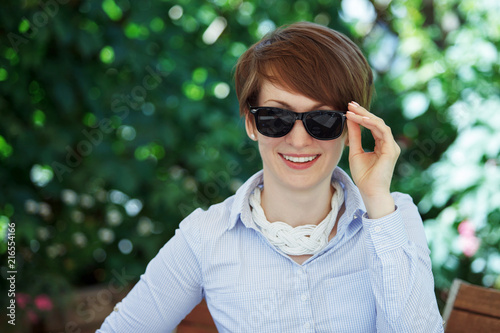 Young cute woman in glasses drinks coffee in a summer cafe.
