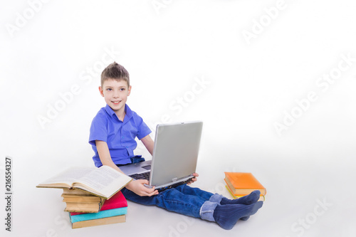 Portrait of cute schoolboy sitting with books and typing on laptop keyboard
