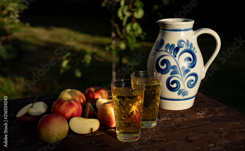 Traditional apple wine in the city of Frankfurt in Hesse. A jug of wine is on an old wooden table in the garden, around it are apples