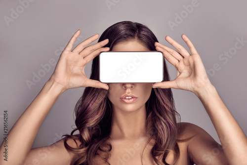 Portrait of pretty woman covering her eyes with smartphone