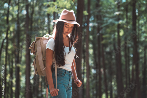 Traveler hipster girl with backpack and hat walking in forest among trees