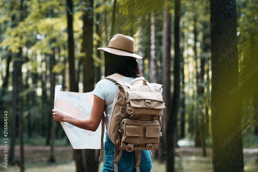 Young traveler woman hold location map in hands among trees in forest and searching directional for traveling Young traveler woman hold location map in hands among trees in forest and searching directional for traveling