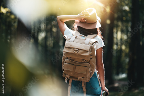 Young woman traveler with backpack walking among trees at forest in sunset photo