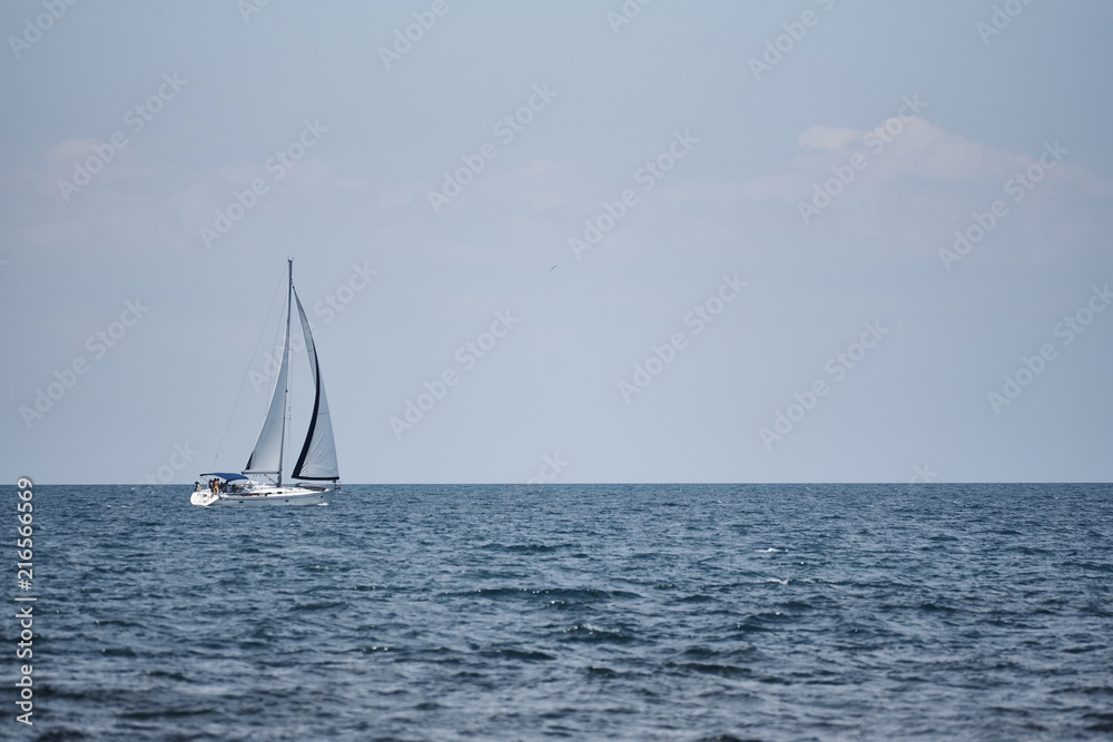 A view of the sea, a white yacht with sails and the sky.