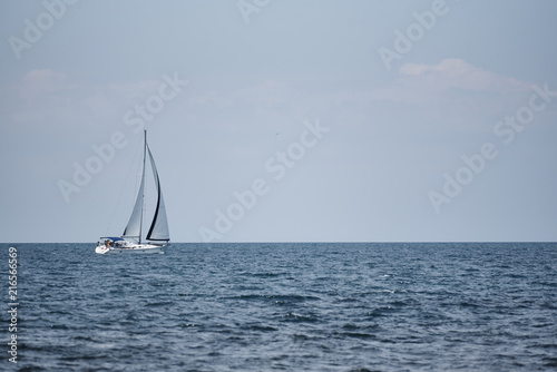 A view of the sea, a white yacht with sails and the sky.