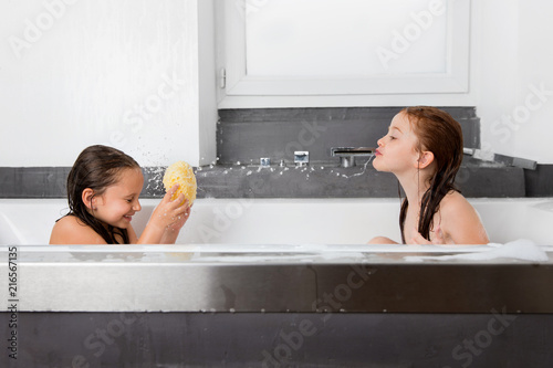 Little girl spitting water at sister in bath photo