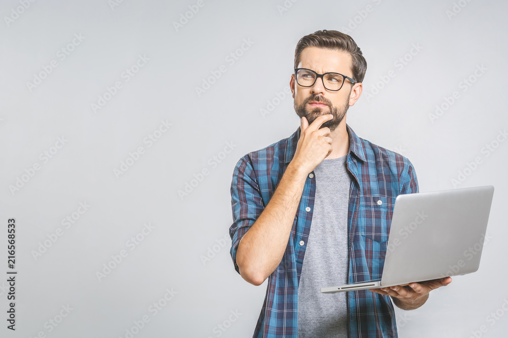 Confident business expert. Confident thoughtful young handsome man in shirt holding laptop while standing against grey background Confident business expert. Confident thoughtful young handsome man in shirt holding laptop while standing against grey background