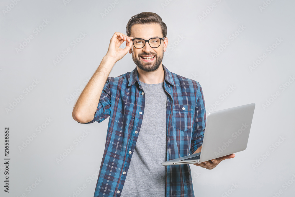 © denis_vermenko - Confident business expert. Confident young handsome man in shirt holding laptop and smiling while standing against grey background © denis_vermenko - Confident business expert. Confident young handsome man in shirt holding laptop and smiling while standing against grey background