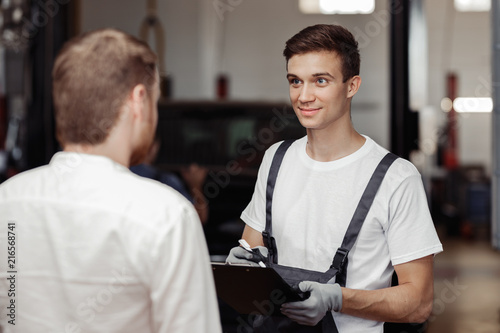 A handsome mechanic is talking to his client about the work done